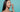 Asian women with dark straight hair applying a white moisturizer to her face in front of a light blue background.
