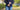 Woman in a blue long sleeve shirt and jeans standing outside holding her hands over her stomach as if she is uncomfortable.