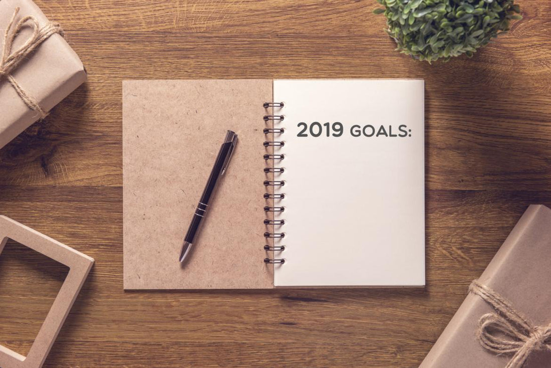 Open notebook laying on a wooden table with the words "2019 goals" printed on the first page.