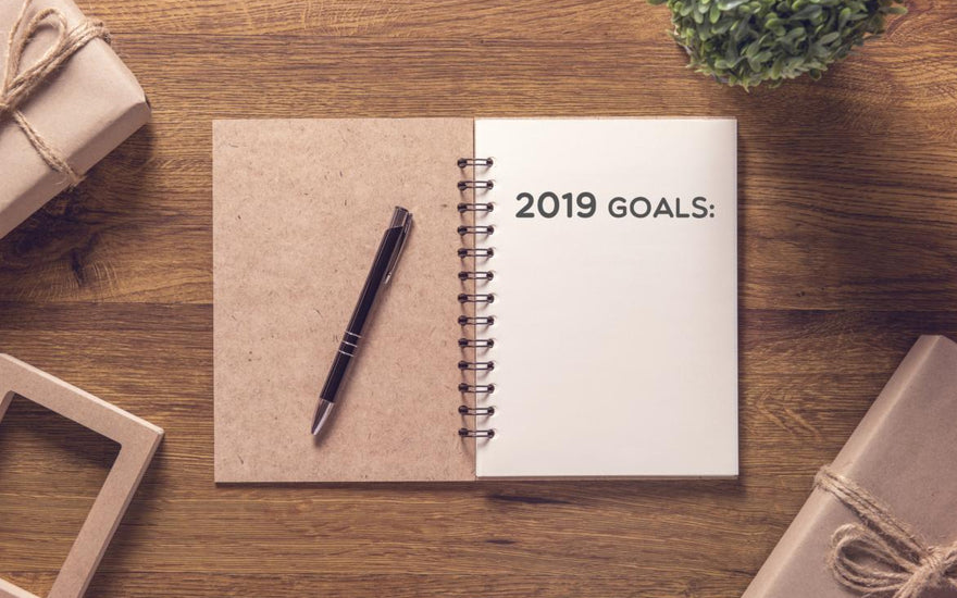 Open notebook laying on a wooden table with the words "2019 goals" printed on the first page.