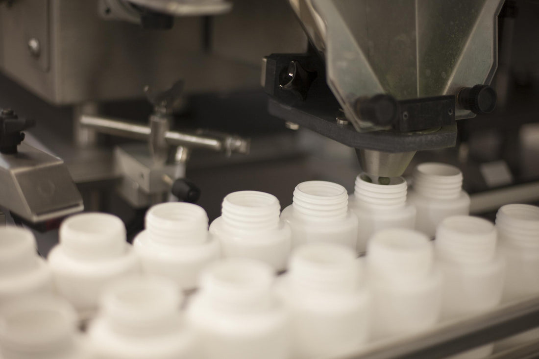 Two lines of white bottles on a machine waiting to be filled with product. 