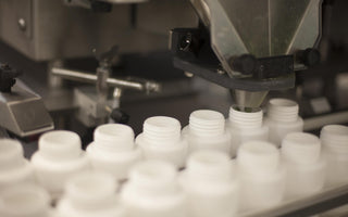 Two lines of white bottles on a machine waiting to be filled with product. 