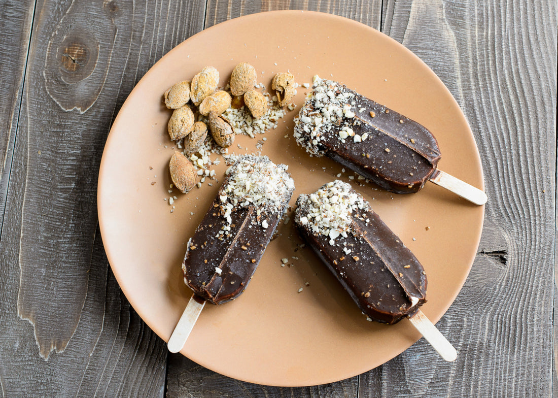 Three fudgesicles topped with coconut shavings sitting on a light brown plate.
