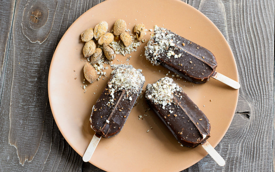 Three fudgesicles topped with coconut shavings sitting on a light brown plate.