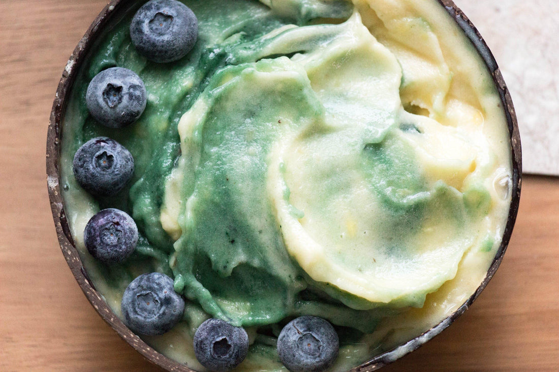 Close up of a smoothie bowl with a green and yellow swirled smoothie topped with blueberries.