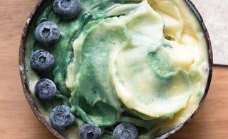 Close up of a smoothie bowl with a green and yellow swirled smoothie topped with blueberries.