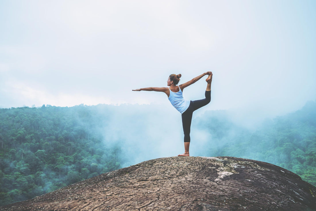 Woman holding a yoga pose on the top of a mountain.
