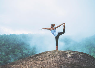 Woman holding a yoga pose on the top of a mountain.