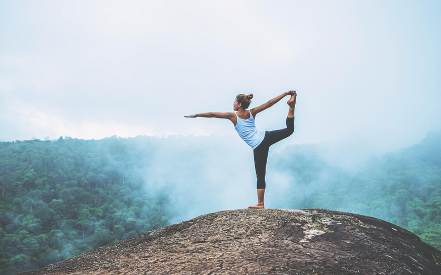 Woman holding a yoga pose on the top of a mountain.