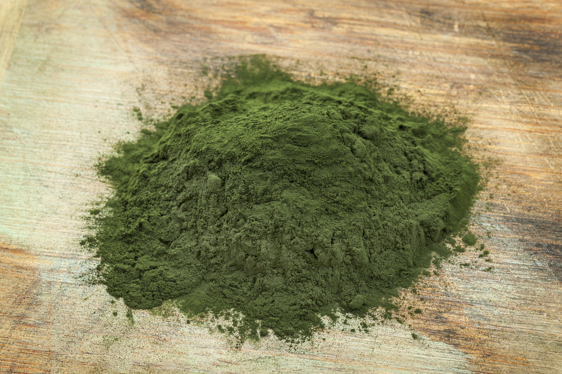 A pile of green algae powder on a wooden tabletop. 