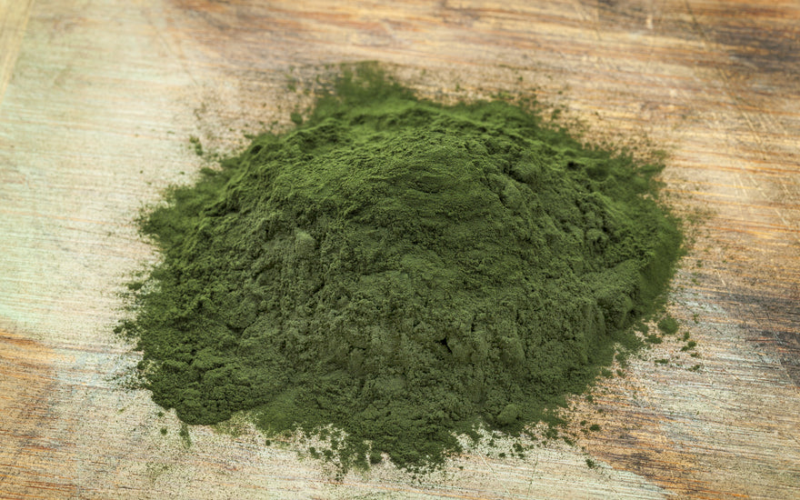 A pile of green algae powder on a wooden tabletop. 