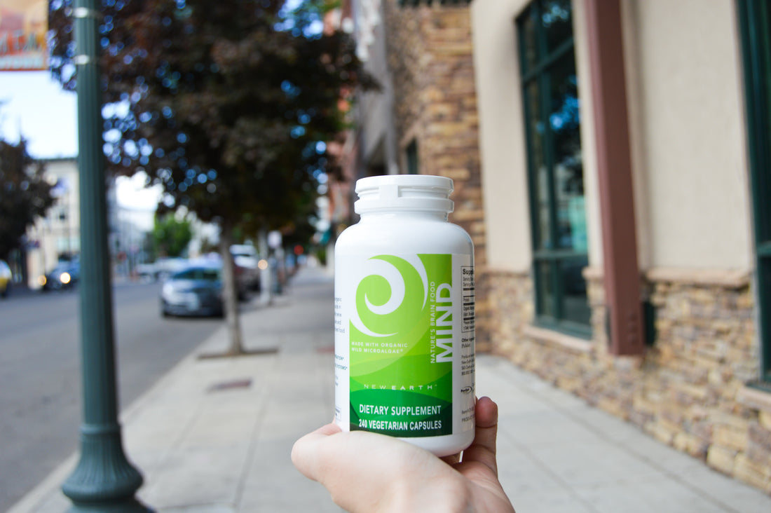 Person's hand holding a bottle of New Earth's Mind on a downtown sidewalk. 