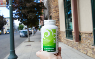 Person's hand holding a bottle of New Earth's Mind on a downtown sidewalk. 