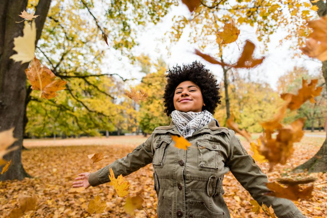 Woman standing with her arms out to her sides as orange autumn leaves fall around her.