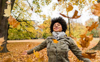 Woman standing with her arms out to her sides as orange autumn leaves fall around her.