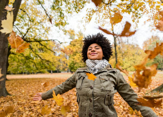 Woman standing with her arms out to her sides as orange autumn leaves fall around her.