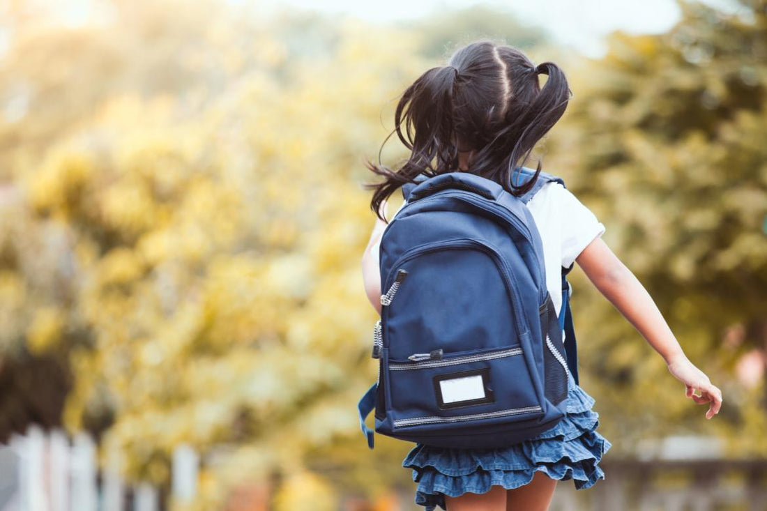 Elementary-aged girl wearing a backpack walking away from the camera on her way to school. 