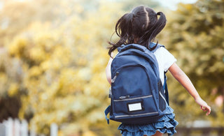 Elementary-aged girl wearing a backpack walking away from the camera on her way to school. 