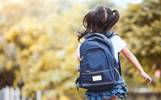 Elementary-aged girl wearing a backpack walking away from the camera on her way to school. 