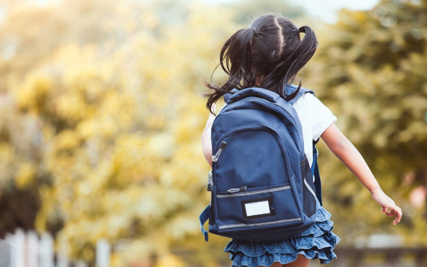 Elementary-aged girl wearing a backpack walking away from the camera on her way to school. 