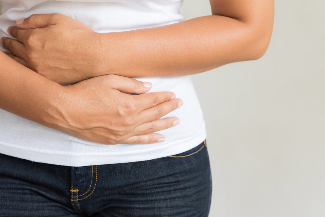 Close up of woman in jeans and a white t-shirt holding her hands over her stomach.