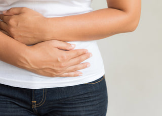 Close up of woman in jeans and a white t-shirt holding her hands over her stomach.