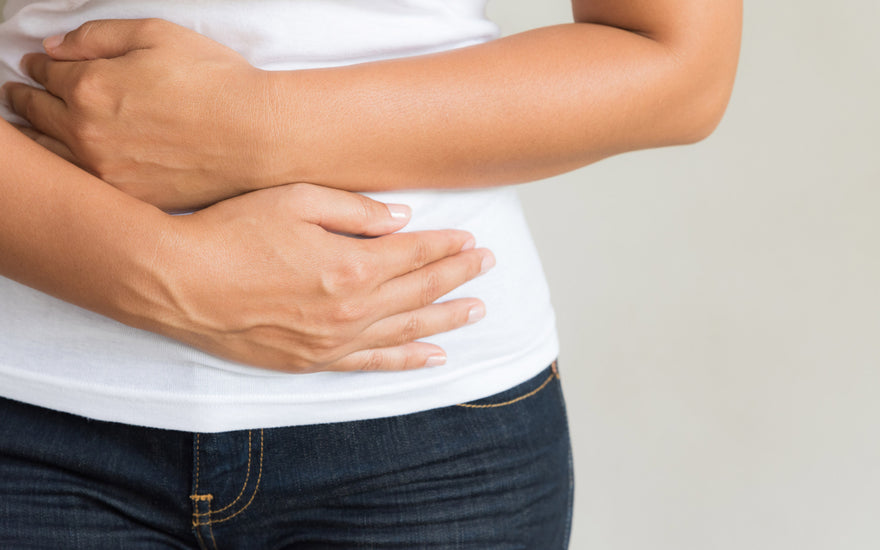 Close up of woman in jeans and a white t-shirt holding her hands over her stomach.