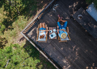 Adult couple sitting in lawn chairs on a deck drinking coffee.