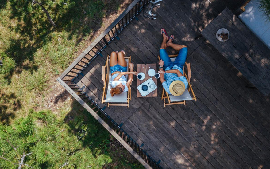 Adult couple sitting in lawn chairs on a deck drinking coffee.