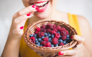 Smiling female in a yellow tank top eating a raspberry from a bowl of mix berries.