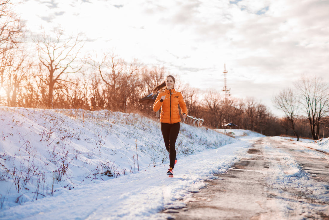 Woman in an orange jacket running along the side of a snowy mountain road. 