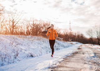 Woman in an orange jacket running along the side of a snowy mountain road. 