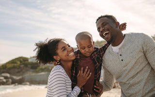 Family of three smiling and laughing while hugging each other outside.