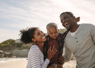 Family of three smiling and laughing while hugging each other outside.