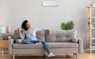 Woman in a grey shirt and jeans sitting relaxed on a grey couch smiling with her eyes closed. 