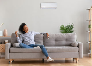 Woman in a grey shirt and jeans sitting relaxed on a grey couch smiling with her eyes closed. 