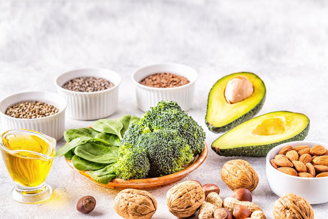 Marble countertop with an array of healthy fat-filled foods like broccoli, nuts, and avocado.