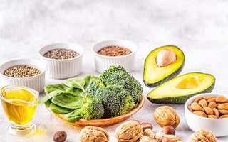 Marble countertop with an array of healthy fat-filled foods like broccoli, nuts, and avocado.