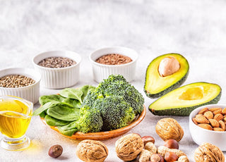 Marble countertop with an array of healthy fat-filled foods like broccoli, nuts, and avocado.