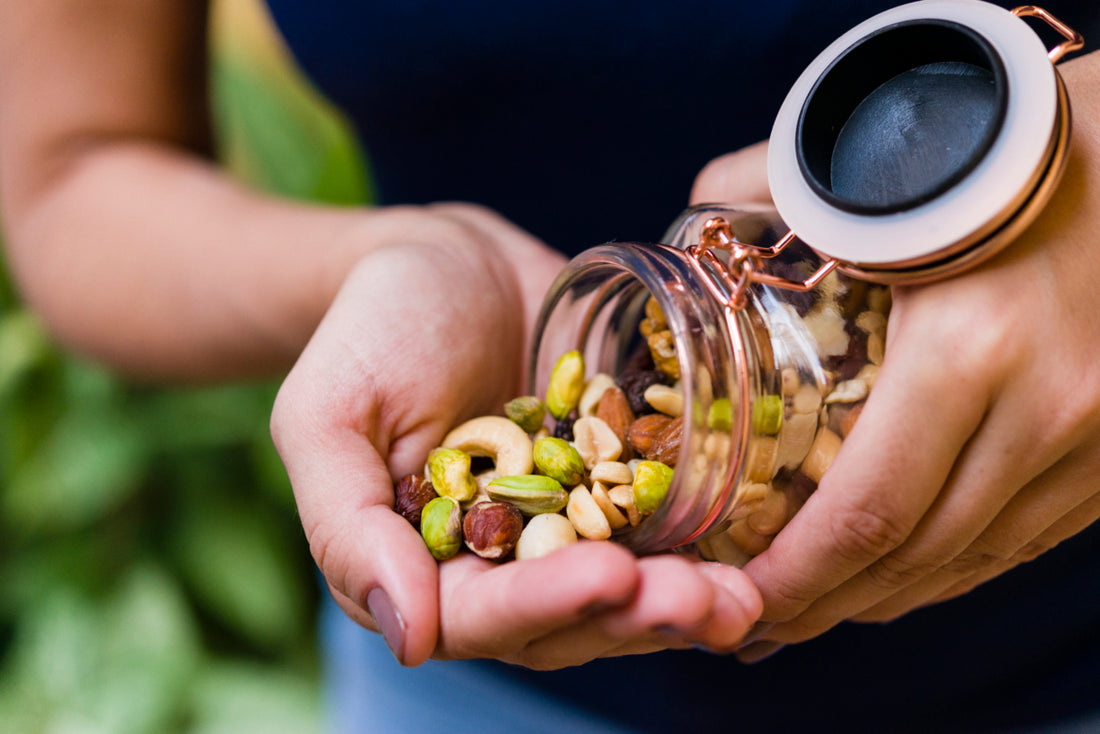 A close-up of a woman pouring a handful of mixed nuts from a glass jar. 