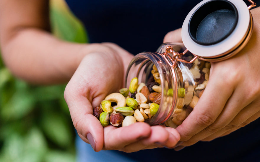 A close-up of a woman pouring a handful of mixed nuts from a glass jar. 