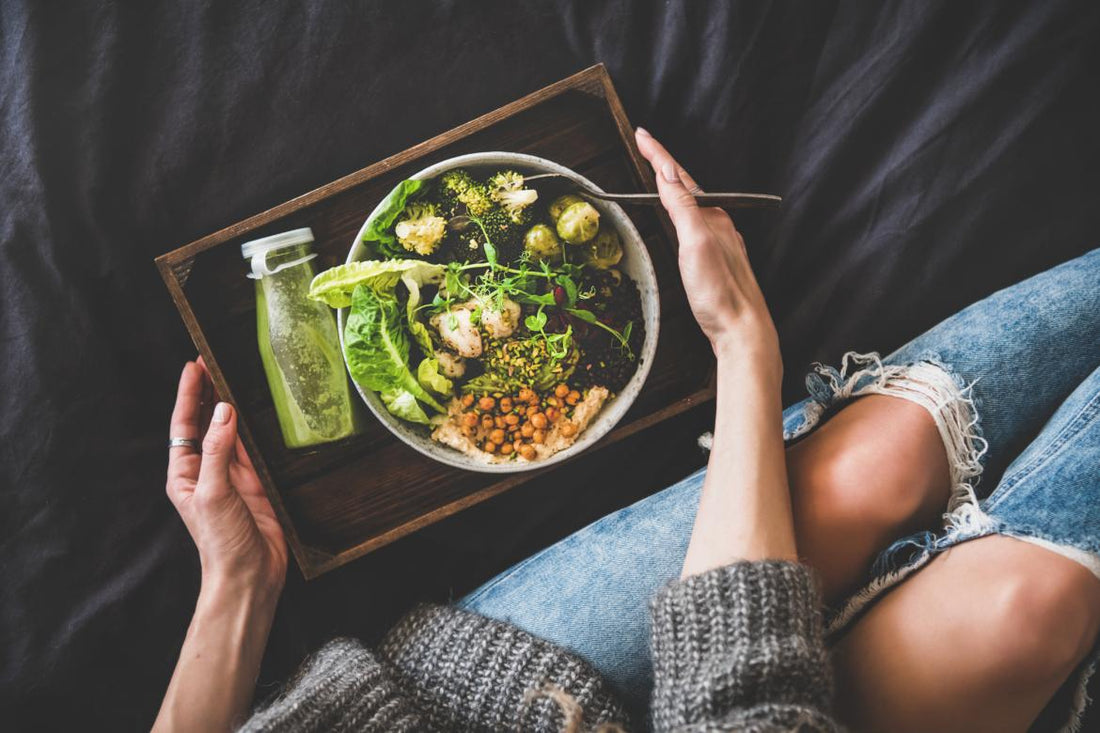 Top down view of a wooden tray with a bottled green drink and a large salad in a bowl on top of it. The tray is being held by the hands of a woman.