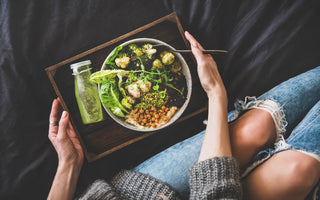 Top down view of a wooden tray with a bottled green drink and a large salad in a bowl on top of it. The tray is being held by the hands of a woman.