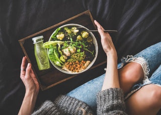 Top down view of a wooden tray with a bottled green drink and a large salad in a bowl on top of it. The tray is being held by the hands of a woman.