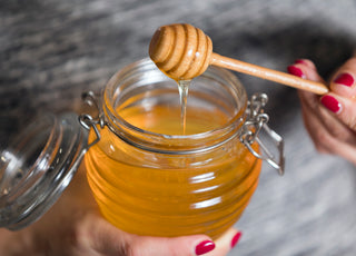 Person holding an open jar of honey.