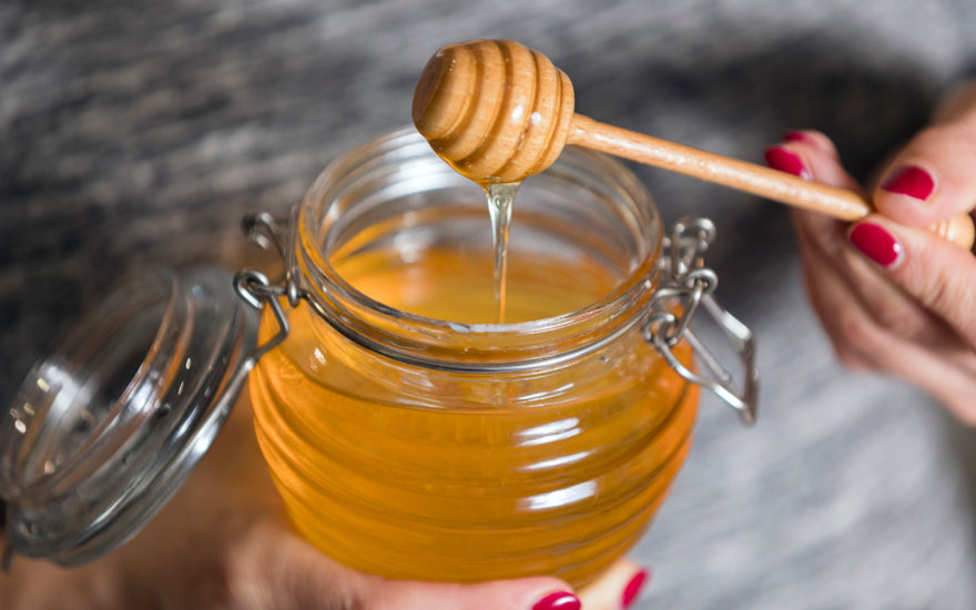 Person holding an open jar of honey.