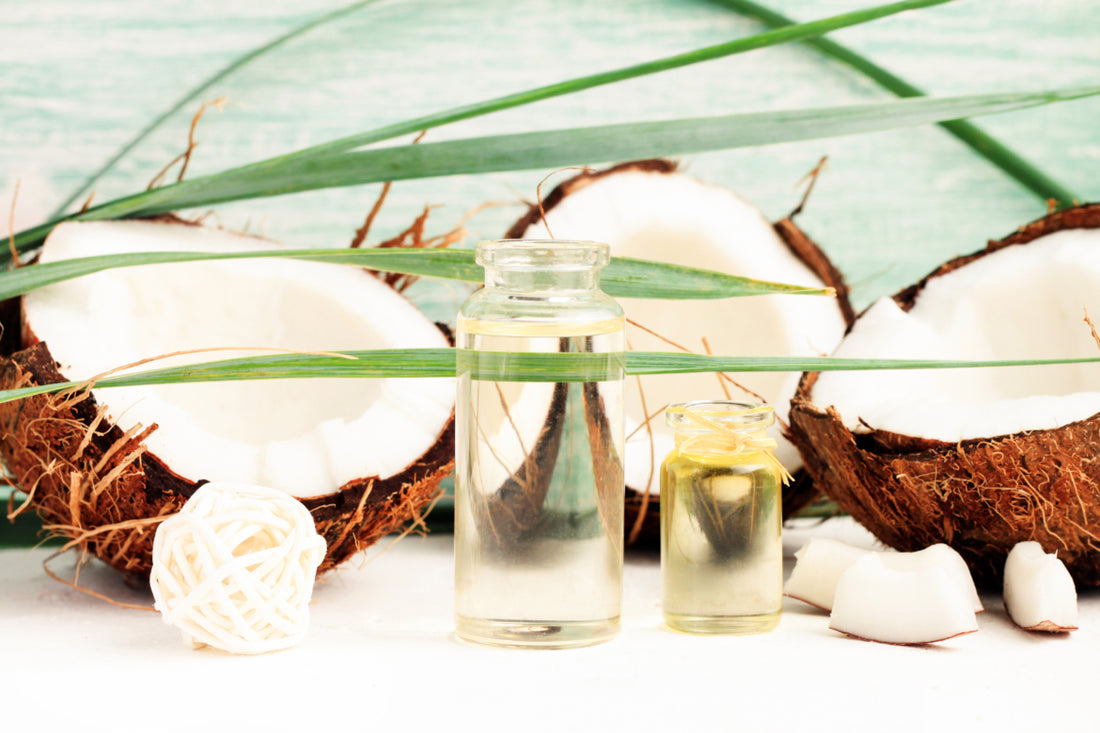 Two small glass jars of coconut oil sitting on a white table next to a few coconuts cut in half.