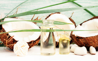 Two small glass jars of coconut oil sitting on a white table next to a few coconuts cut in half.