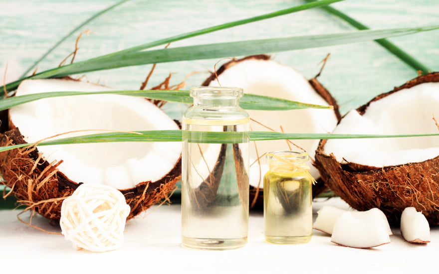 Two small glass jars of coconut oil sitting on a white table next to a few coconuts cut in half.