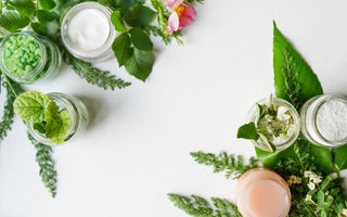 Plant-based skincare ingredients in jars sitting on a table surrounded by greenery.